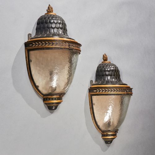 fig 1. A pair of early 19th-century French tole peinte wall lanterns featuring imbricated scale domes, flame finials, and parcel gilt leaf borders over curved textured glass.