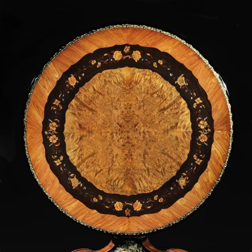 fig 3. A 19th-century circular marquetry centre table featuring floral wood inlays, a tilt-top mechanism, and a dark carved tripod base with gilt-bronze mounts.