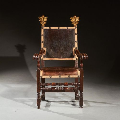 fig 1. A pair of seventeenth-century Italian Baroque walnut armchairs featuring dark brown leather upholstery, decorative brass studs, turned stretchers, and gilded acanthus leaf finials.