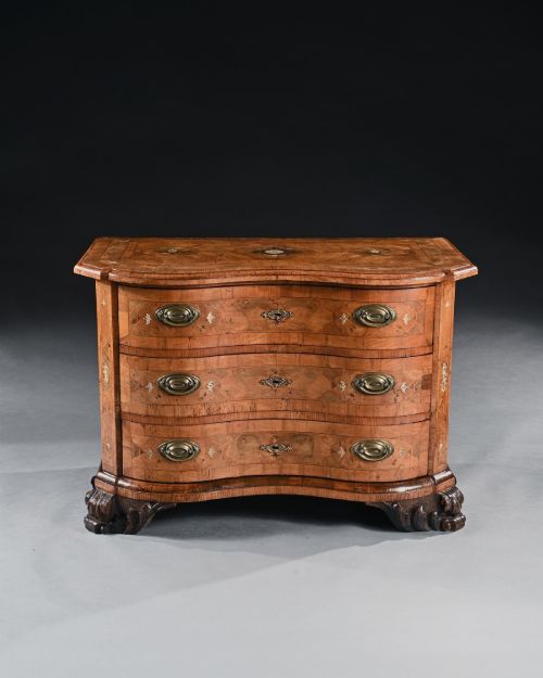 fig 1. A mid-eighteenth-century German serpentine walnut commode featuring three drawers decorated with metal marquetry inlays, brass handles, and carved corner feet.