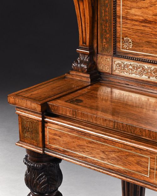fig 2. A Regency rosewood writing table featuring intricate brass scrollwork inlay, an anthemion top gallery, a central frieze drawer, and carved reeded legs.
