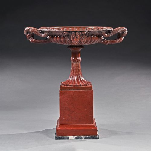fig 1. A carved deep red Rosso Antico marble tazza featuring serpent handles, a Medusa mask motif, and a fluted stem set upon a square pedestal base.