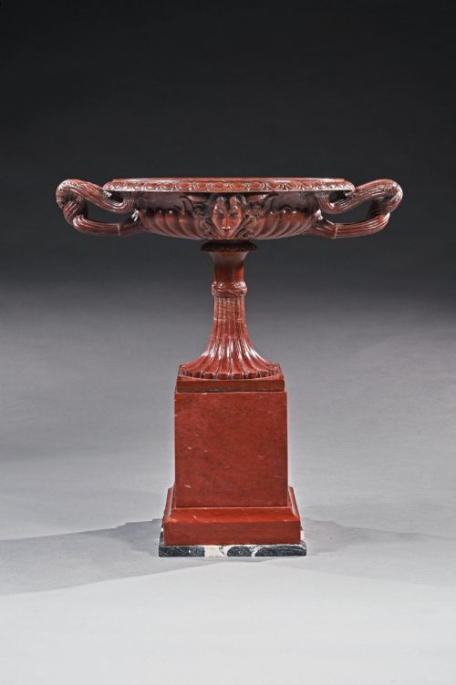 fig 3. A carved deep red Rosso Antico marble tazza featuring serpent handles, a Medusa mask motif, and a fluted stem set upon a square pedestal base.