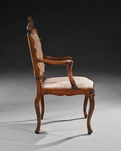fig 1. Mid-18th-century Italian Rococo carved walnut armchair featuring cabriole legs, curved armrests, an ornate carved mask crest rail, and exposed traditional back padding.