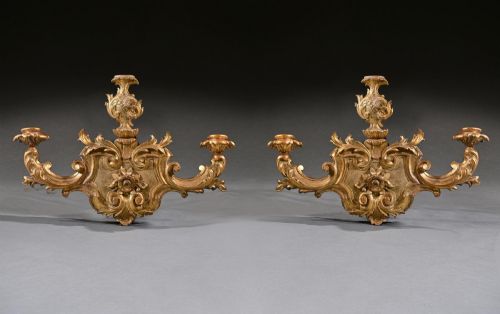 fig 1. A pair of carved giltwood wall sconces featuring ornate rococo scrollwork, acanthus leaf motifs, and twin candle arms against a dark backdrop.