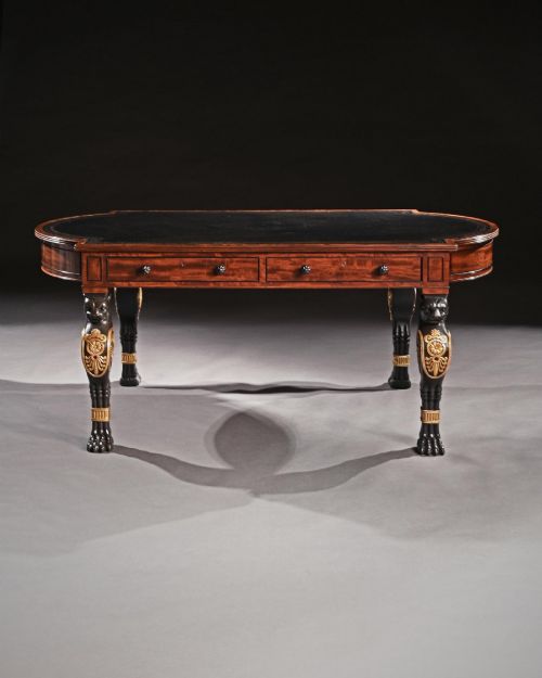 fig 3. A Regency style mahogany writing table featuring a dark leather inset top, frieze drawers, and four ebonised monopodia legs ornamented with carved lion heads and gilt accents.