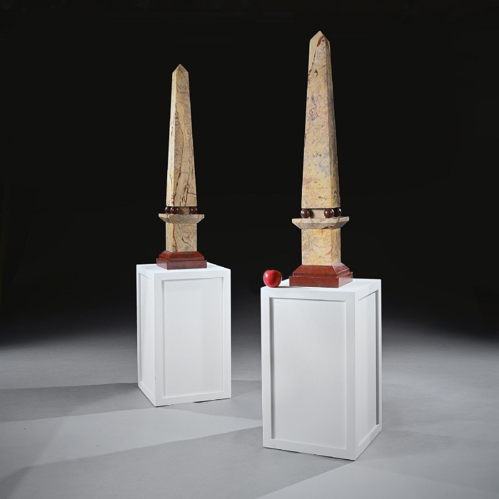 A pair of tall Portasanta marble obelisks featuring cream and brown veining, resting on spherical red marble feet and stepped Rosso Antico bases.