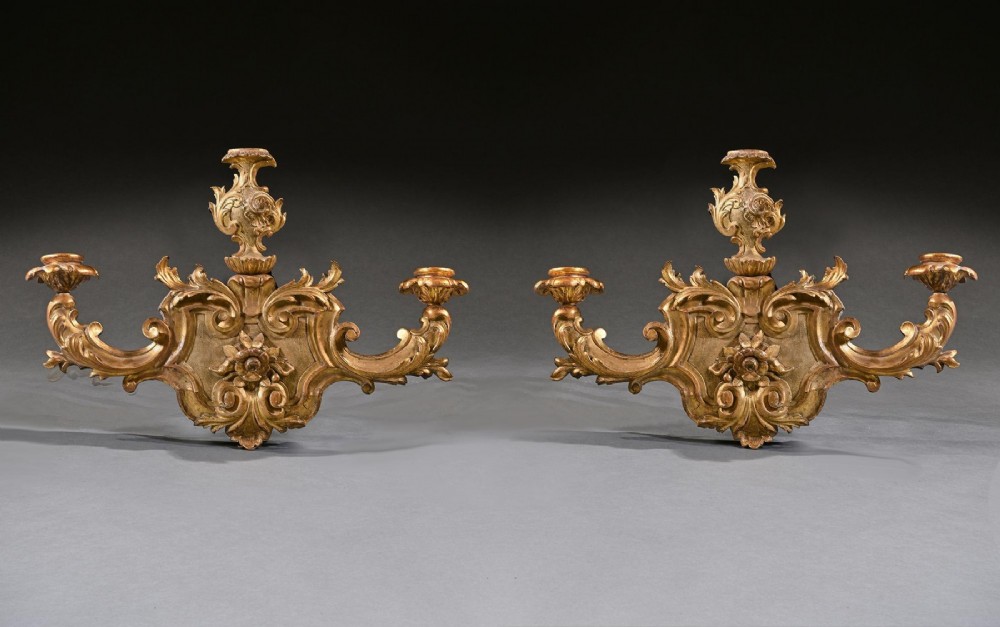 A pair of 18th-century Venetian carved giltwood wall sconces decorated with Rococo scrollwork, central urn finials, and candle nozzles. View II