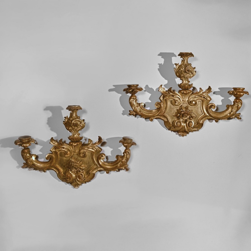 A pair of 18th-century Venetian carved giltwood wall sconces decorated with Rococo scrollwork, central urn finials, and candle nozzles. View V