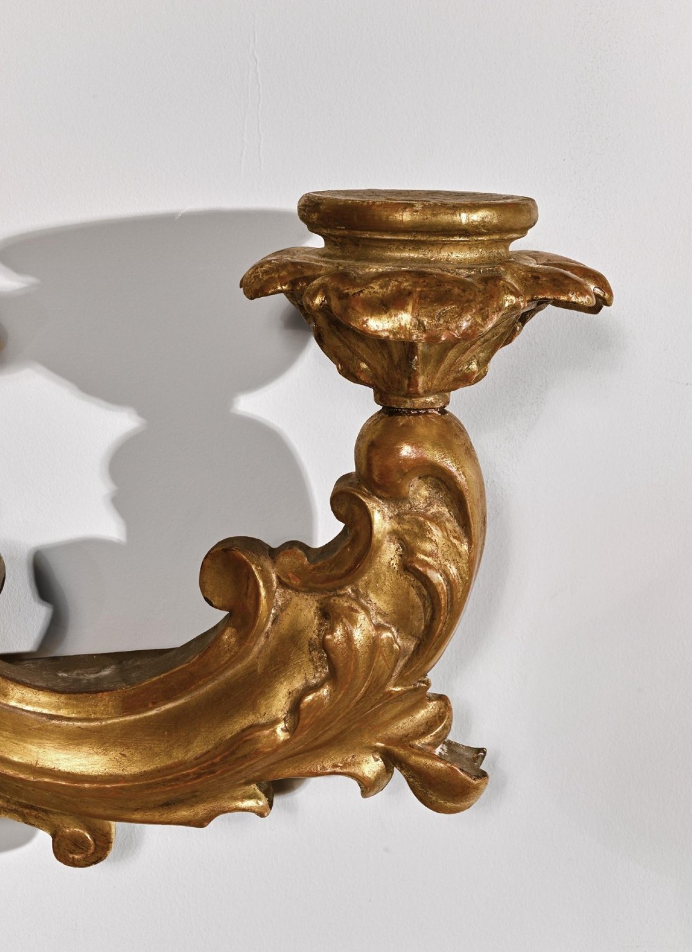 A pair of 18th-century Venetian carved giltwood wall sconces decorated with Rococo scrollwork, central urn finials, and candle nozzles. View VI