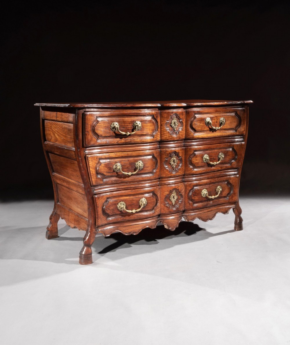 A mid-18th-century Louis XV French provincial chestnut commode featuring a bombe profile, three carved drawers, and brass hardware. View III