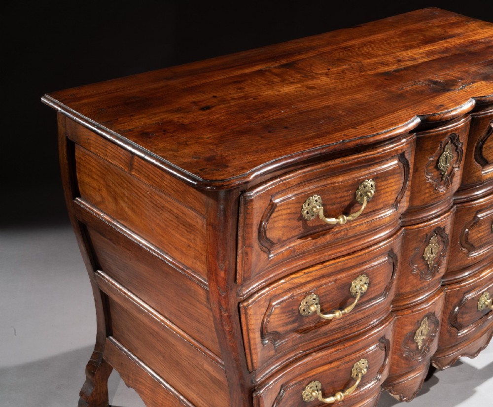 A mid-18th-century Louis XV French provincial chestnut commode featuring a bombe profile, three carved drawers, and brass hardware. View IV