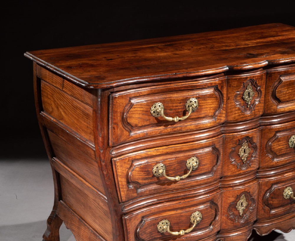 A mid-18th-century Louis XV French provincial chestnut commode featuring a bombe profile, three carved drawers, and brass hardware. View V