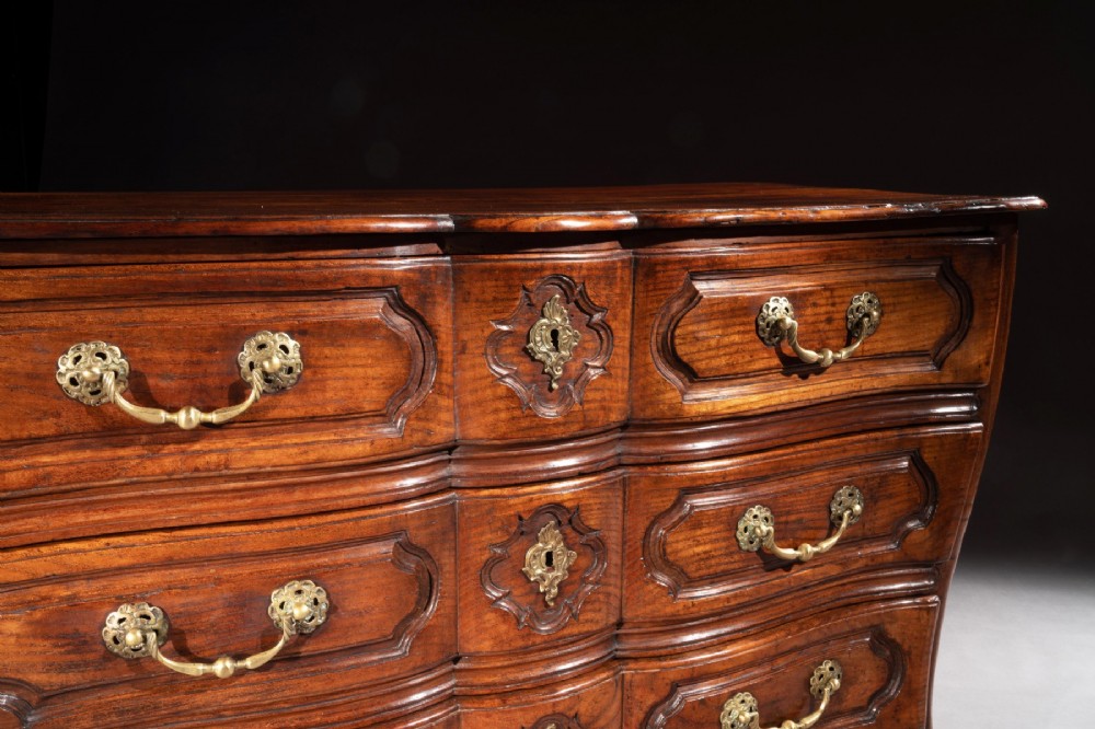 A mid-18th-century Louis XV French provincial chestnut commode featuring a bombe profile, three carved drawers, and brass hardware. View VI