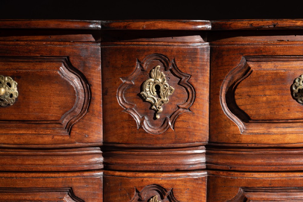 A mid-18th-century Louis XV French provincial chestnut commode featuring a bombe profile, three carved drawers, and brass hardware. View IX