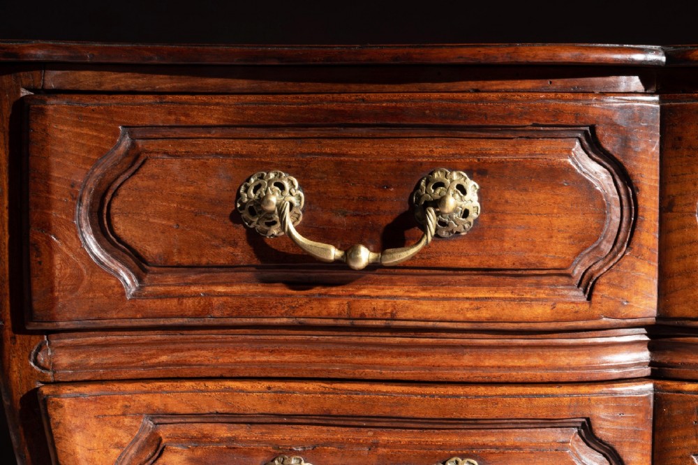 A mid-18th-century Louis XV French provincial chestnut commode featuring a bombe profile, three carved drawers, and brass hardware. View X