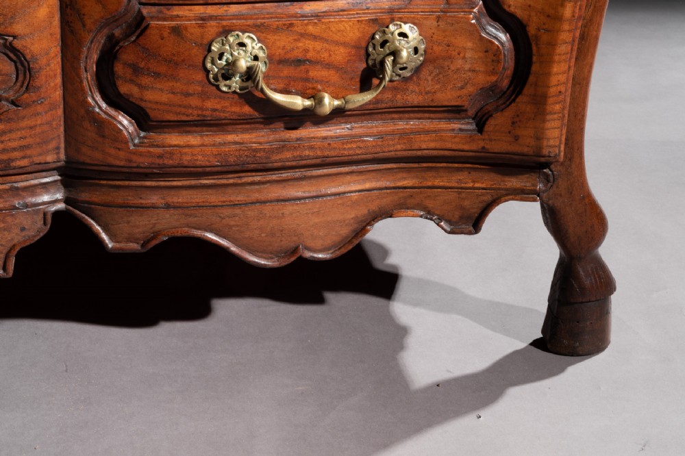 A mid-18th-century Louis XV French provincial chestnut commode featuring a bombe profile, three carved drawers, and brass hardware. View XI