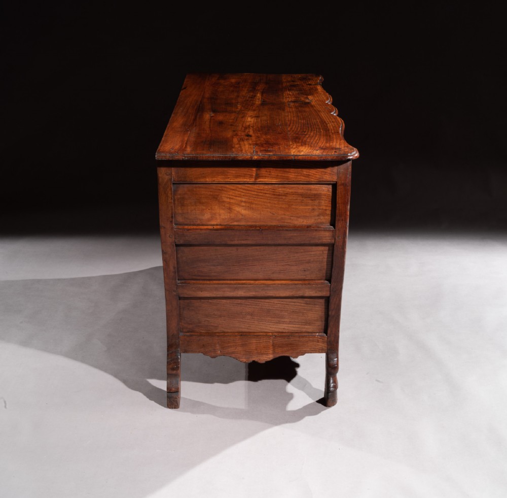 A mid-18th-century Louis XV French provincial chestnut commode featuring a bombe profile, three carved drawers, and brass hardware. View XII