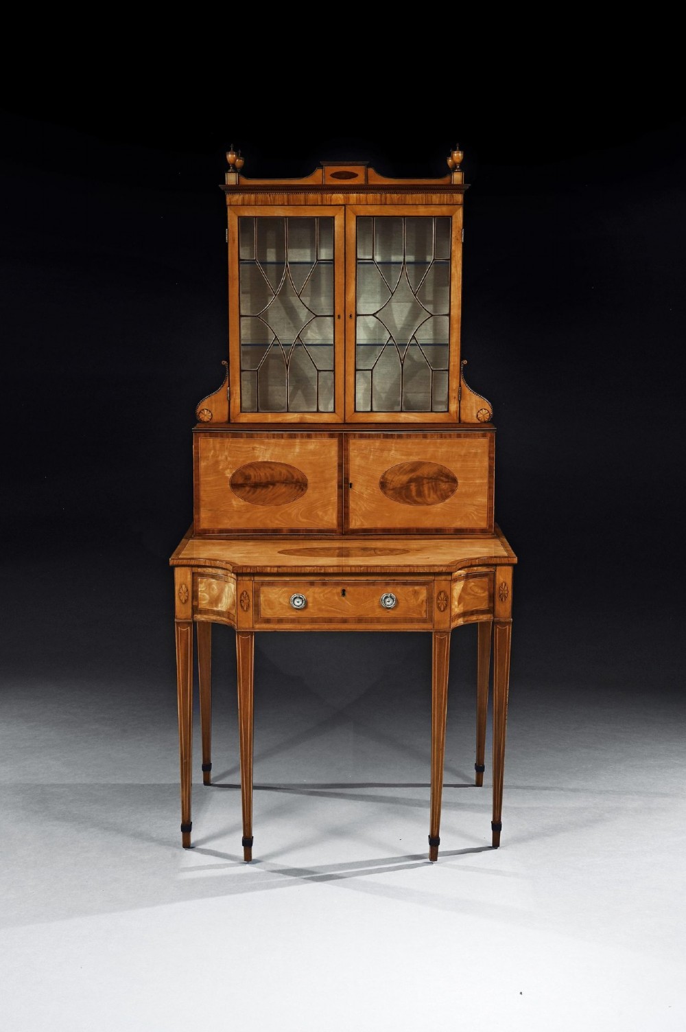 An 18th-century George III satinwood writing cabinet with a glazed upper bookcase, oval inlaid cupboard doors, and slender tapered legs. View V