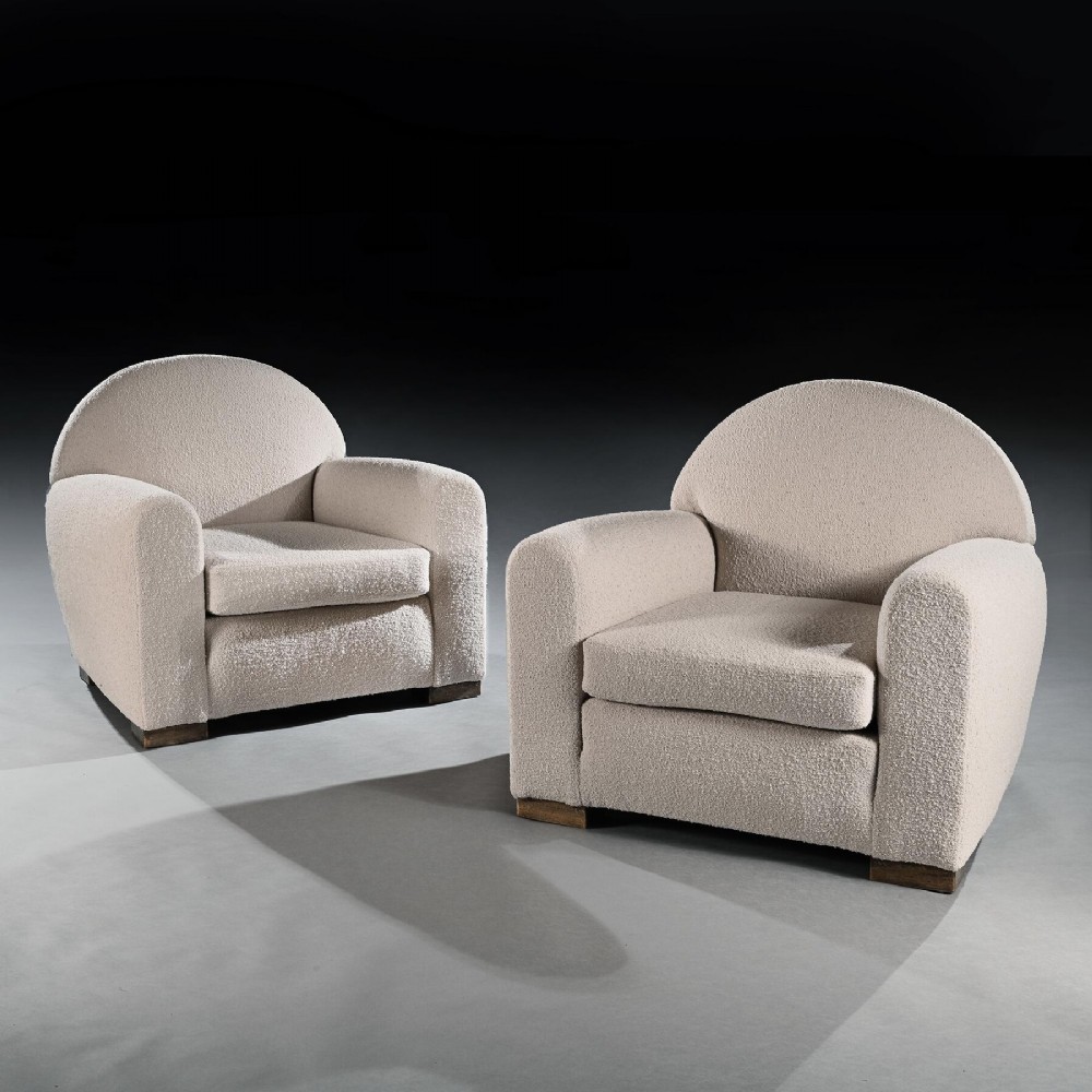 A pair of mid-twentieth-century French club armchairs upholstered in cream boucle fabric with rounded backrests and low wooden block feet.