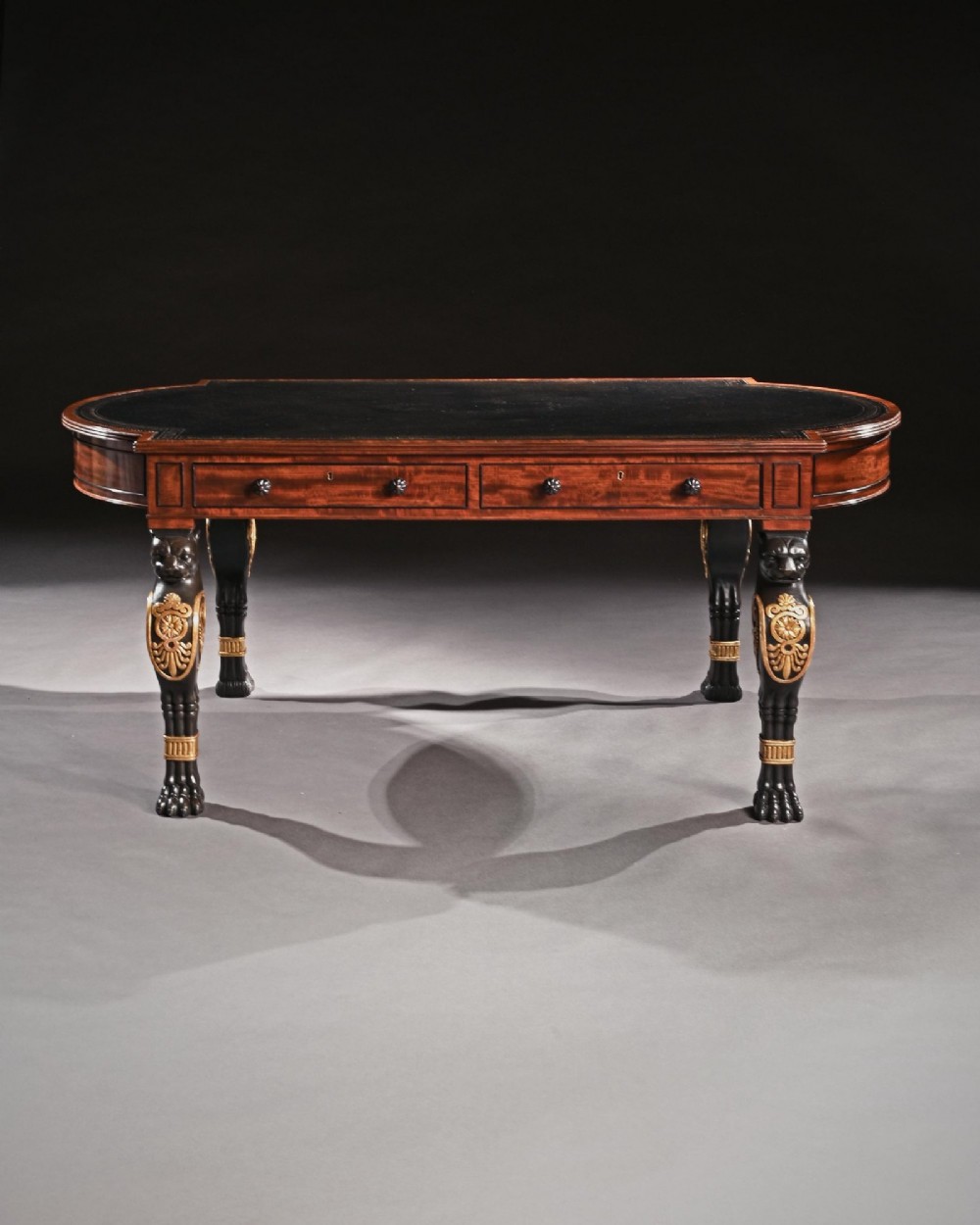 A Regency mahogany partners writing table with a dark leather inset top, frieze drawers, and ebonised lion monopodia legs adorned with gilt highlights. View IV