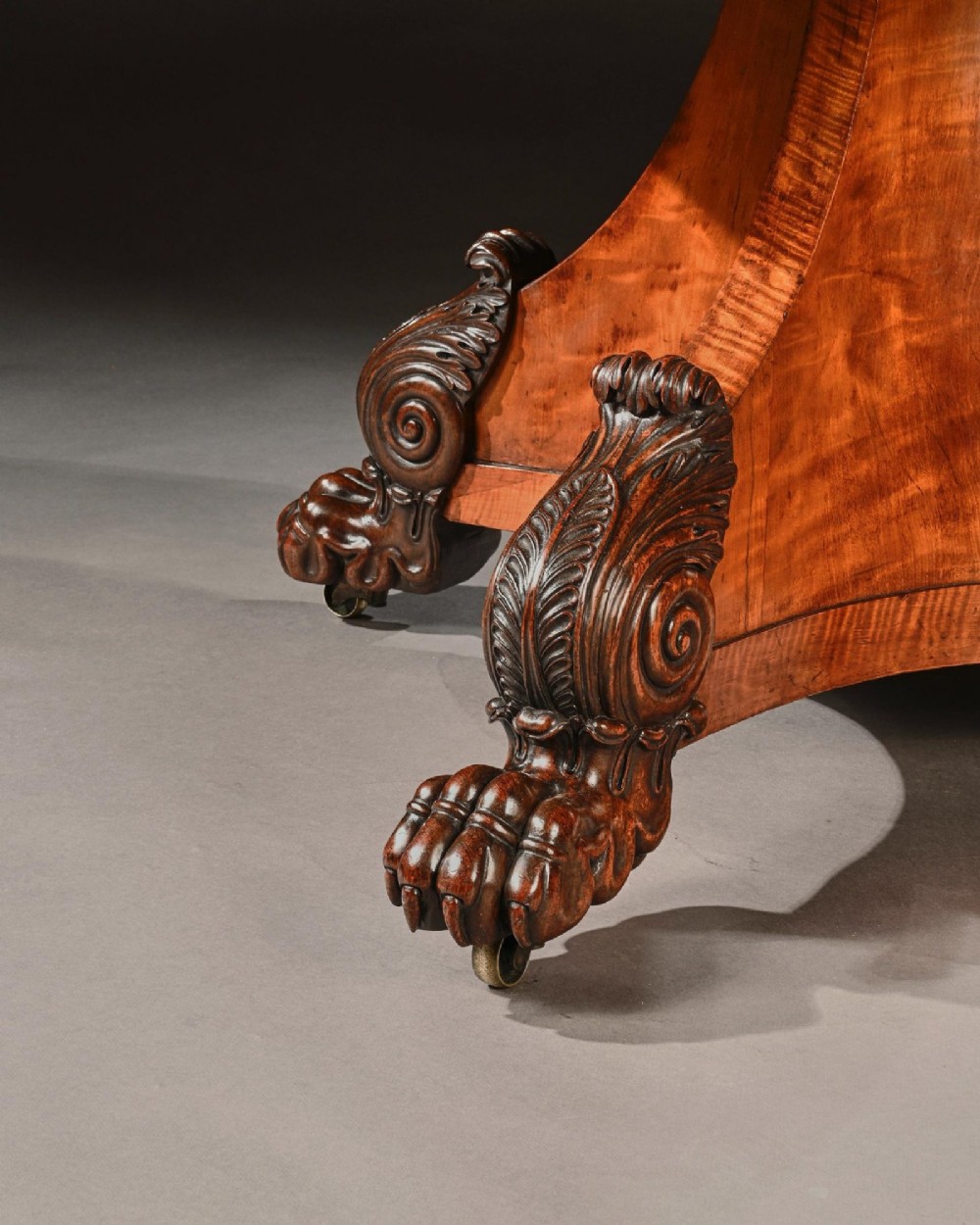 A nineteenth-century circular satinwood centre table featuring rosewood crossbanding, a central pedestal support, and a carved triform base with paw feet on castors. View VI
