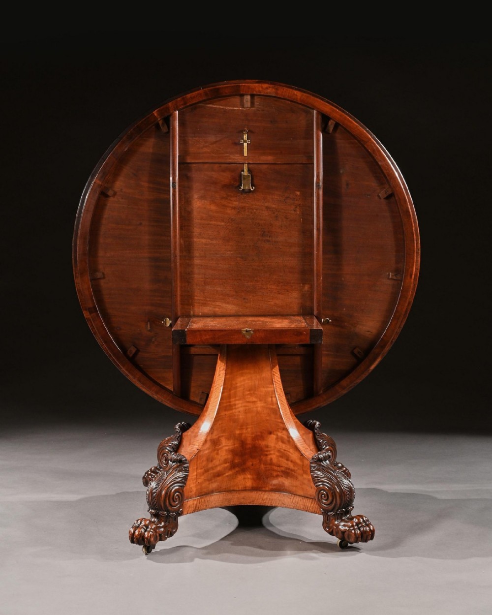 A nineteenth-century circular satinwood centre table featuring rosewood crossbanding, a central pedestal support, and a carved triform base with paw feet on castors. View VIII