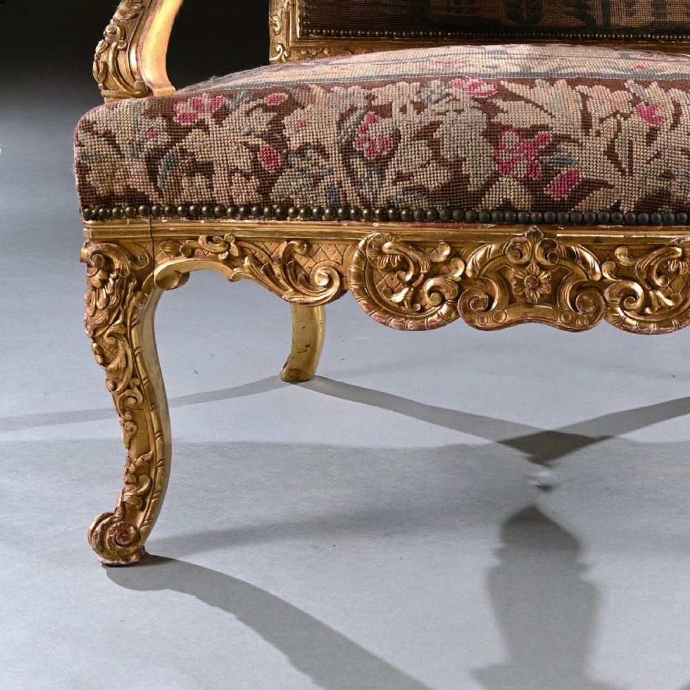An 18th-century French Regence giltwood armchair featuring ornate shell carving, cabriole legs, and tapestry upholstery depicting figures and floral motifs. View V