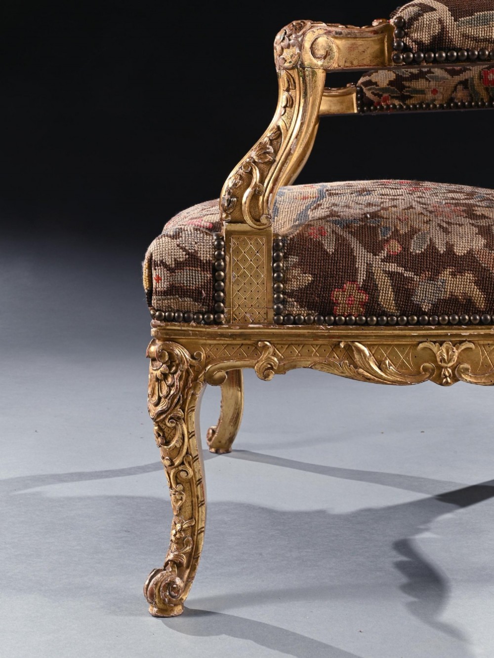 An 18th-century French Regence giltwood armchair featuring ornate shell carving, cabriole legs, and tapestry upholstery depicting figures and floral motifs. View VI