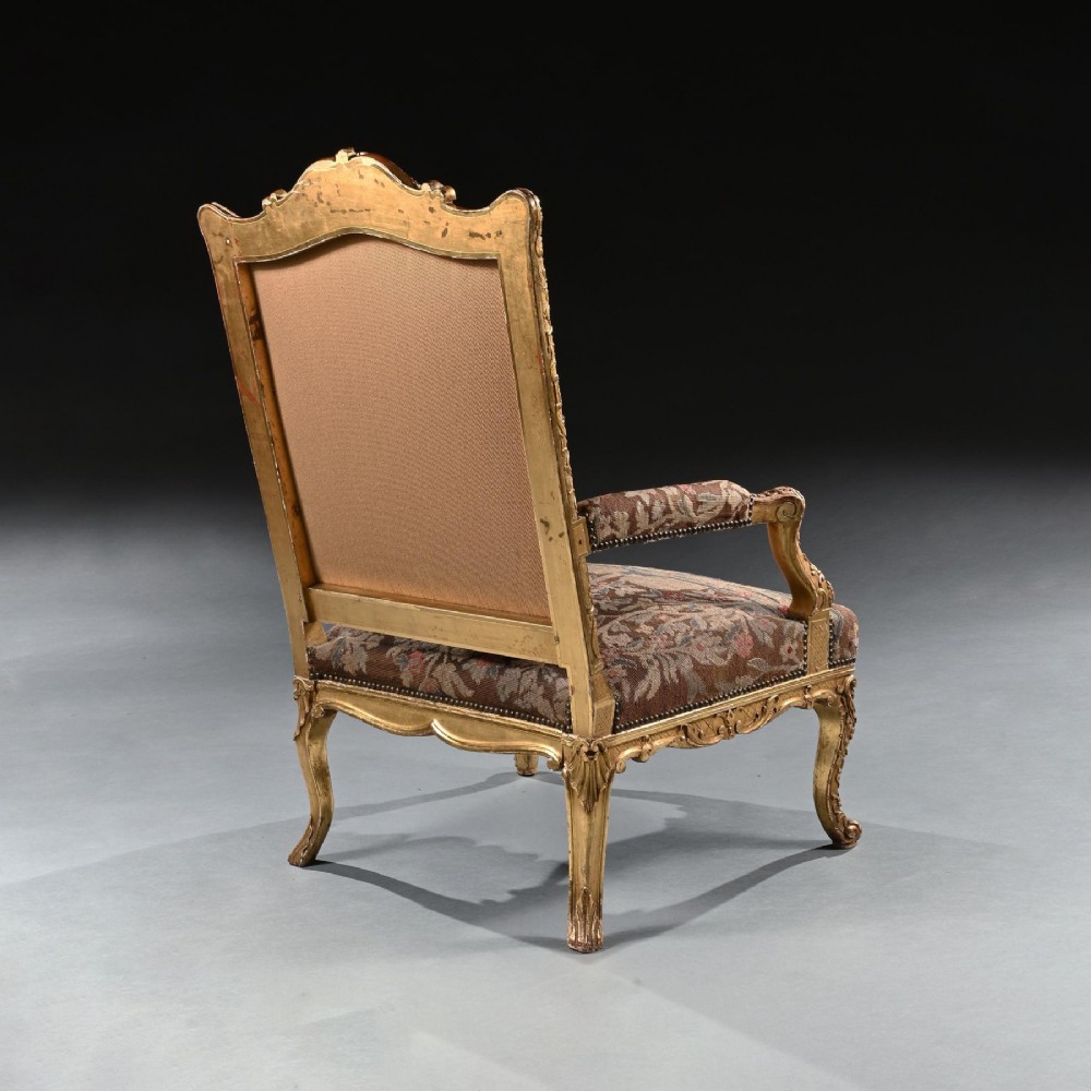 An 18th-century French Regence giltwood armchair featuring ornate shell carving, cabriole legs, and tapestry upholstery depicting figures and floral motifs. View VII