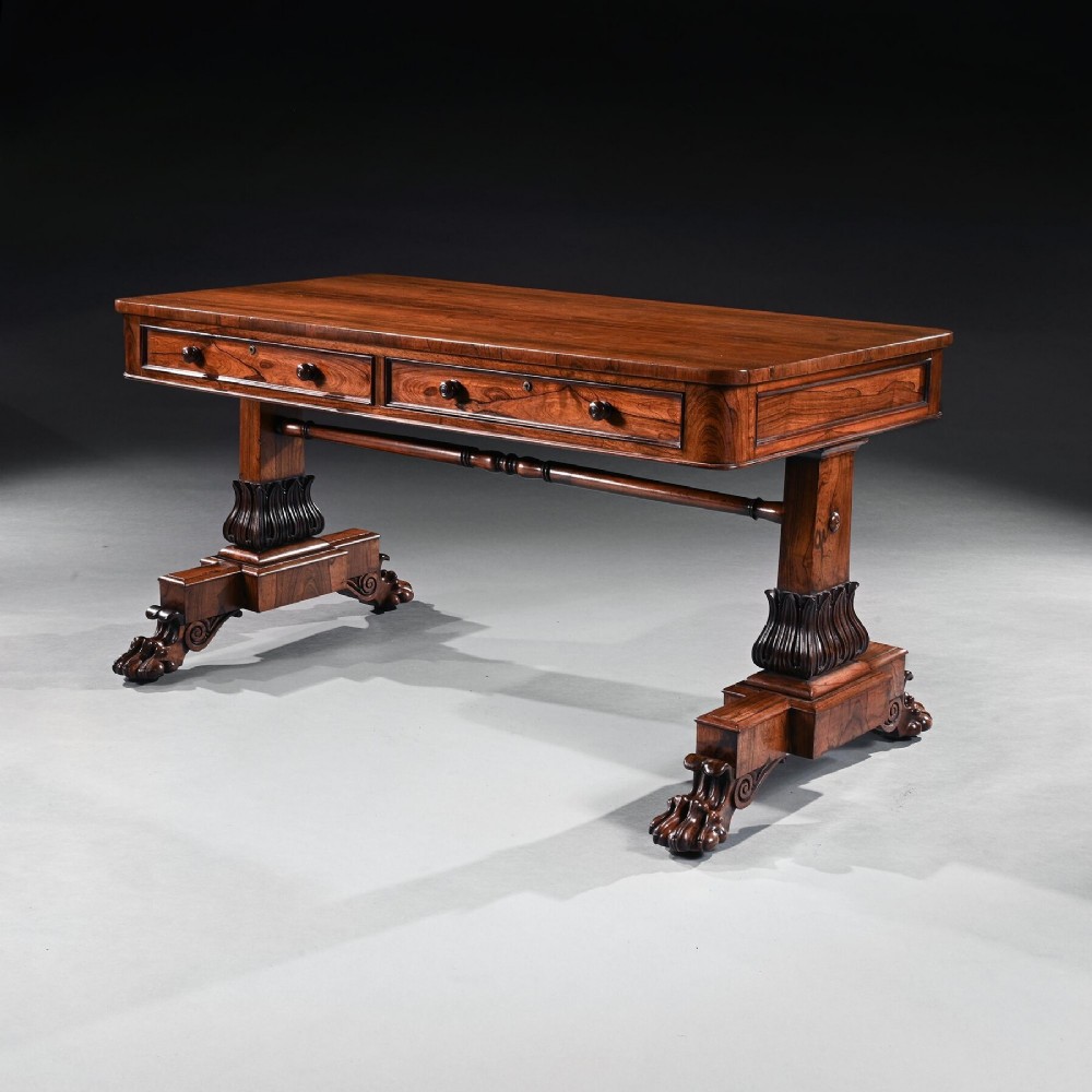 A George IV period rosewood library table featuring two frieze drawers, a turned central stretcher, and pedestal supports ending in carved lions paw feet.