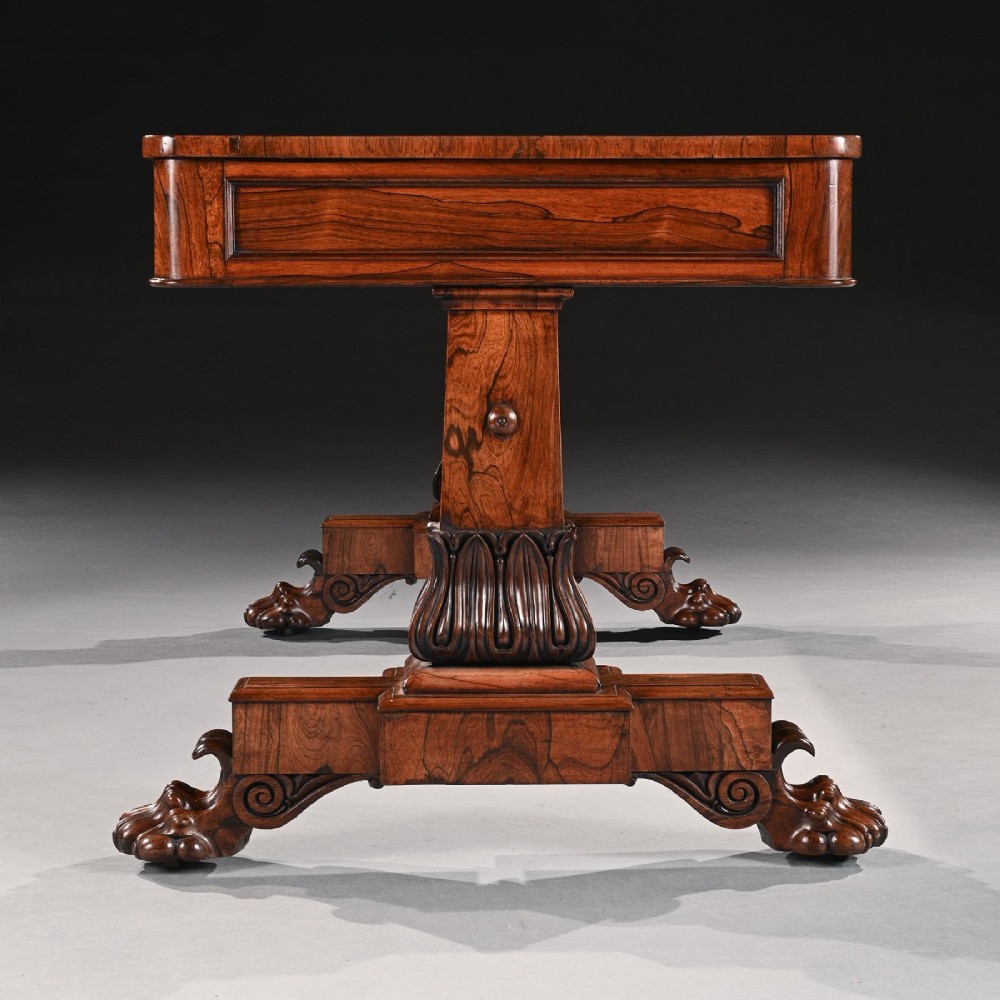 A George IV period rosewood library table featuring two frieze drawers, a turned central stretcher, and pedestal supports ending in carved lions paw feet. View IV