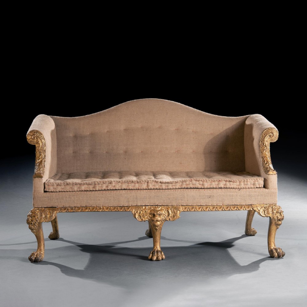 A George II carved giltwood sofa upholstered in neutral beige fabric, supported on six cabriole legs featuring carved lion mask knees and hairy paw feet. View II