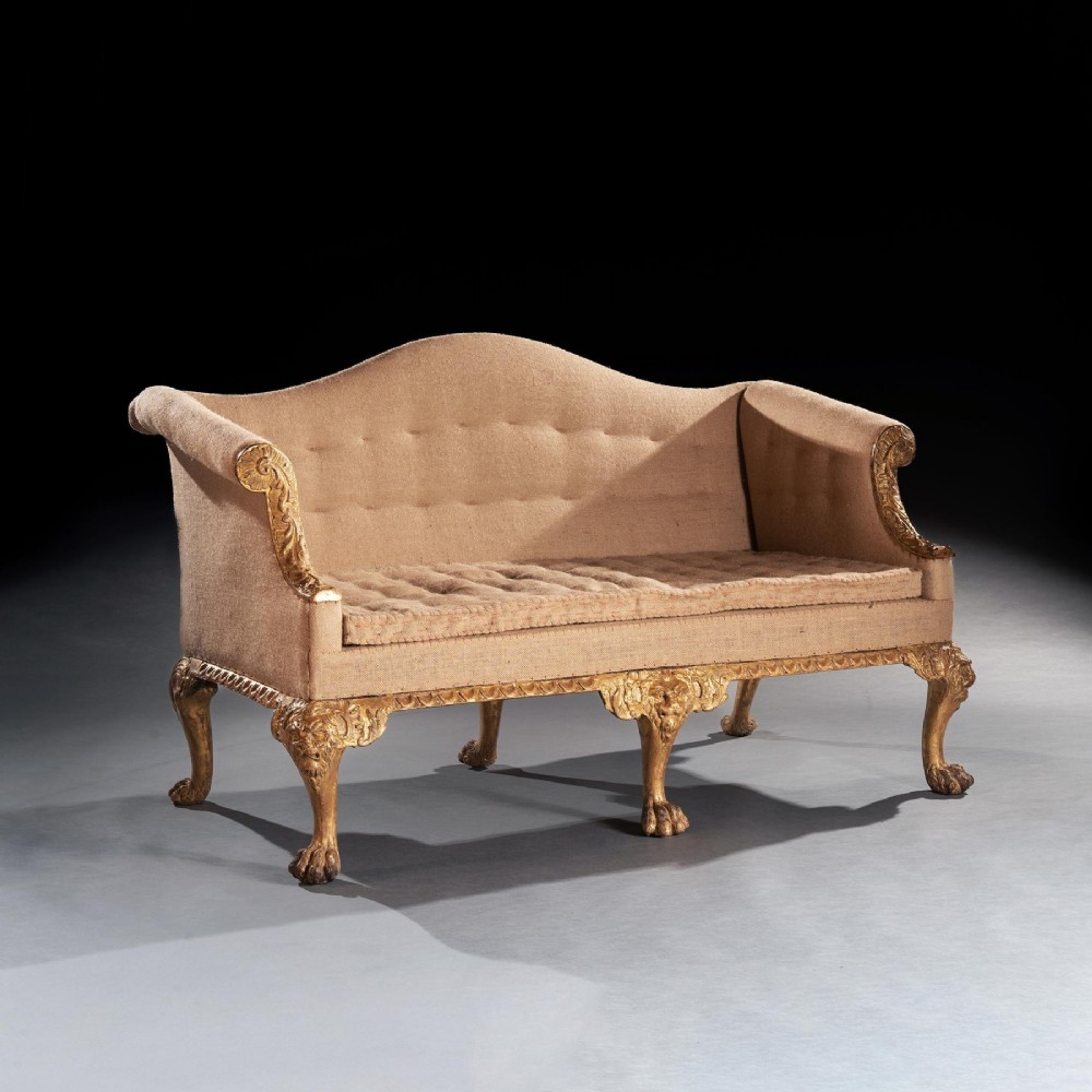 A George II carved giltwood sofa upholstered in neutral beige fabric, supported on six cabriole legs featuring carved lion mask knees and hairy paw feet. View III