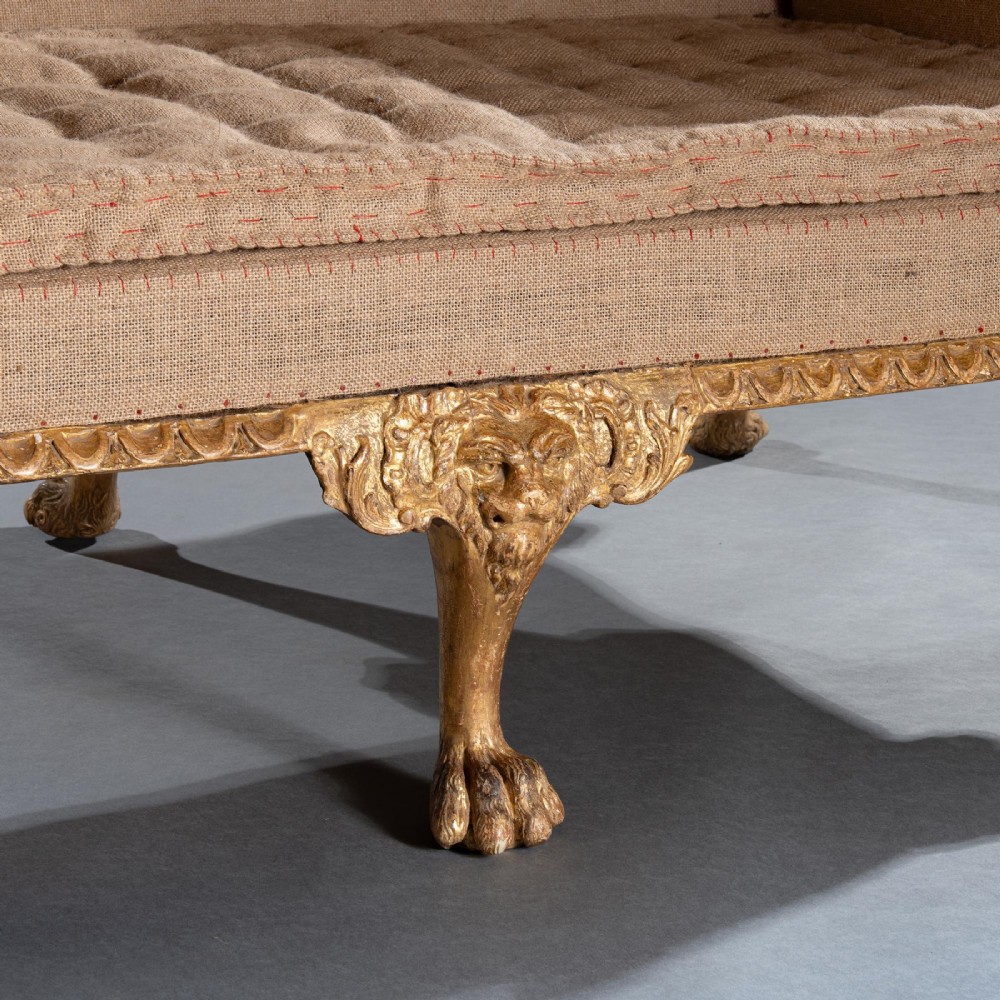 A George II carved giltwood sofa upholstered in neutral beige fabric, supported on six cabriole legs featuring carved lion mask knees and hairy paw feet. View V