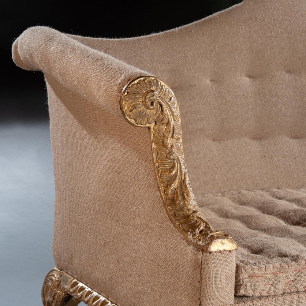 A George II carved giltwood sofa upholstered in neutral beige fabric, supported on six cabriole legs featuring carved lion mask knees and hairy paw feet. View VI