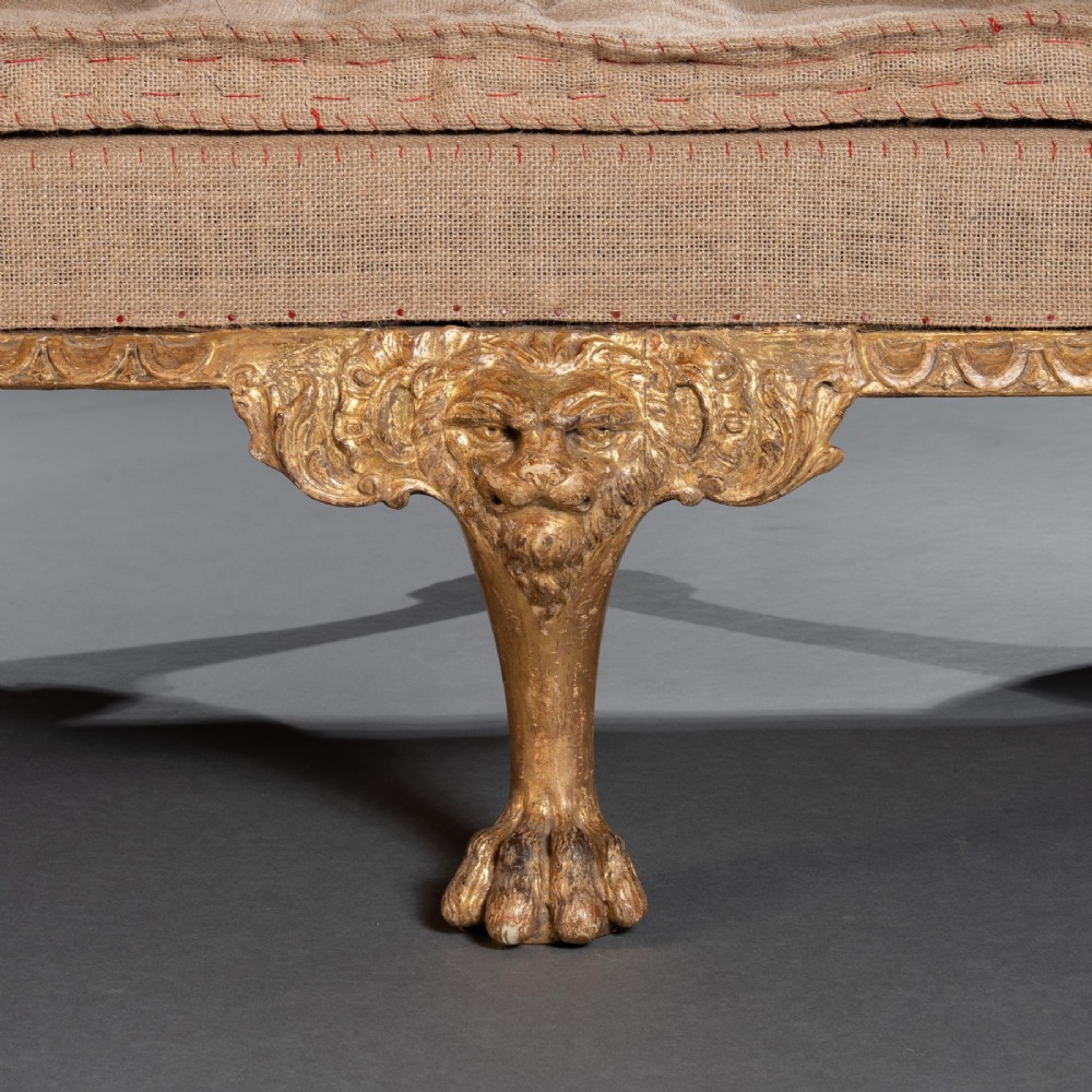 A George II carved giltwood sofa upholstered in neutral beige fabric, supported on six cabriole legs featuring carved lion mask knees and hairy paw feet. View VII