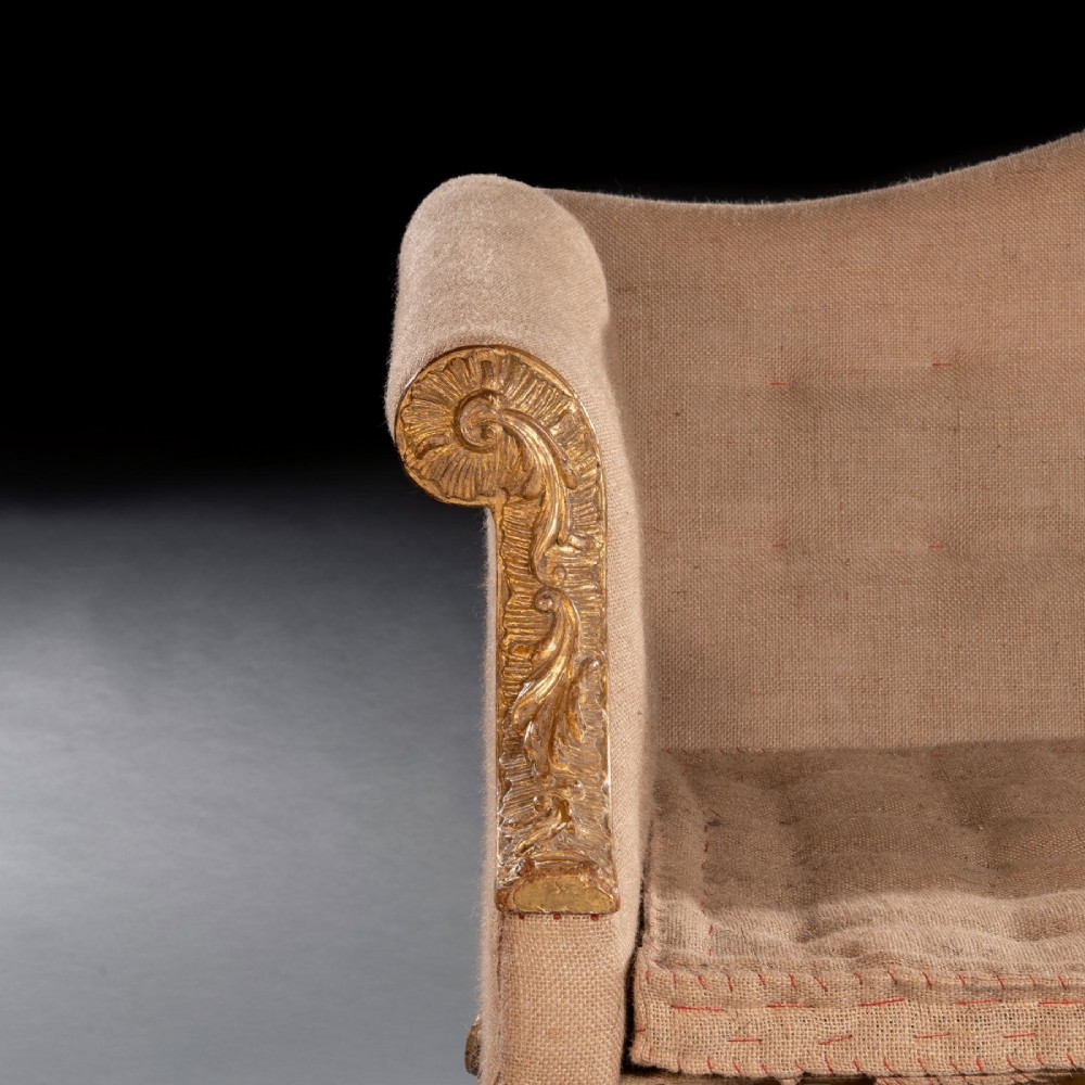 A George II carved giltwood sofa upholstered in neutral beige fabric, supported on six cabriole legs featuring carved lion mask knees and hairy paw feet. View VIII