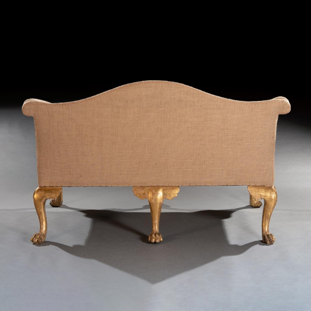 A George II carved giltwood sofa upholstered in neutral beige fabric, supported on six cabriole legs featuring carved lion mask knees and hairy paw feet. View X