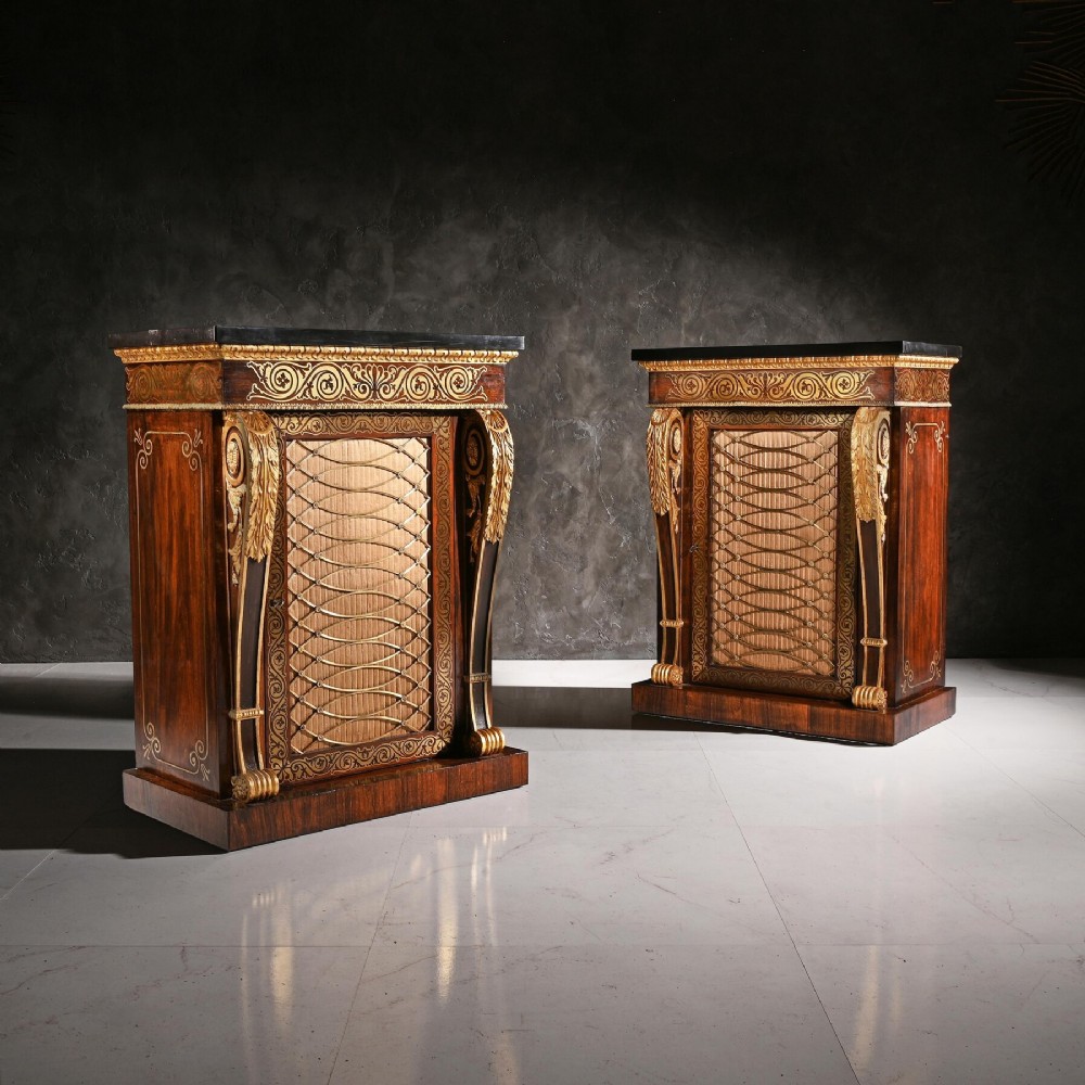 A pair of dark wood Regency side cabinets featuring intricate brass inlaid foliage, gilt corner mounts, brass wire mesh doors, and dark marble tops.
