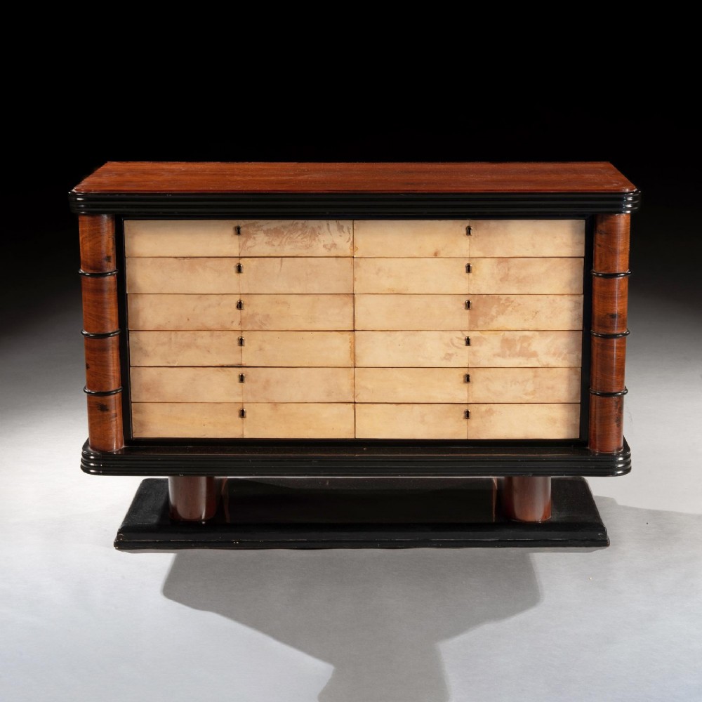 An Art Deco palisander commode featuring twelve parchment-covered drawer fronts, ebonised side trim, curved timber flanks, and a stepped plinth base. View II
