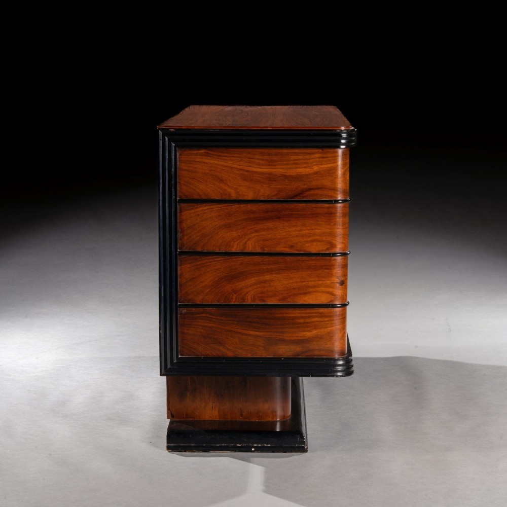 An Art Deco palisander commode featuring twelve parchment-covered drawer fronts, ebonised side trim, curved timber flanks, and a stepped plinth base. View VIII