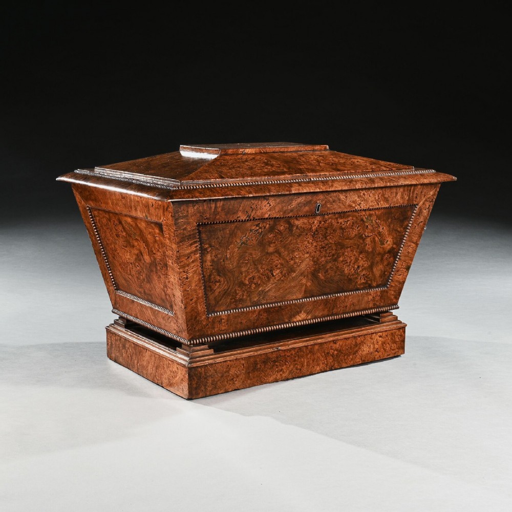 A George IV sarcophagus-shaped cellarette crafted from figured pollard oak with a stepped lid and beaded moulding on a plinth base.