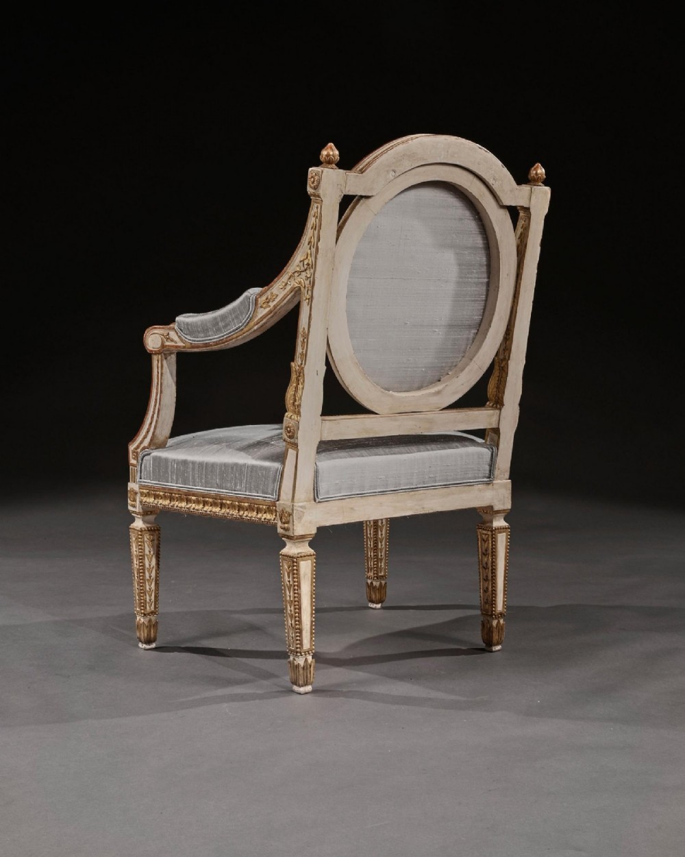 A pair of 19th-century Italian Neoclassical armchairs featuring cream painted and gilt carved frames, oval backrests, and light grey silk upholstery. View VI