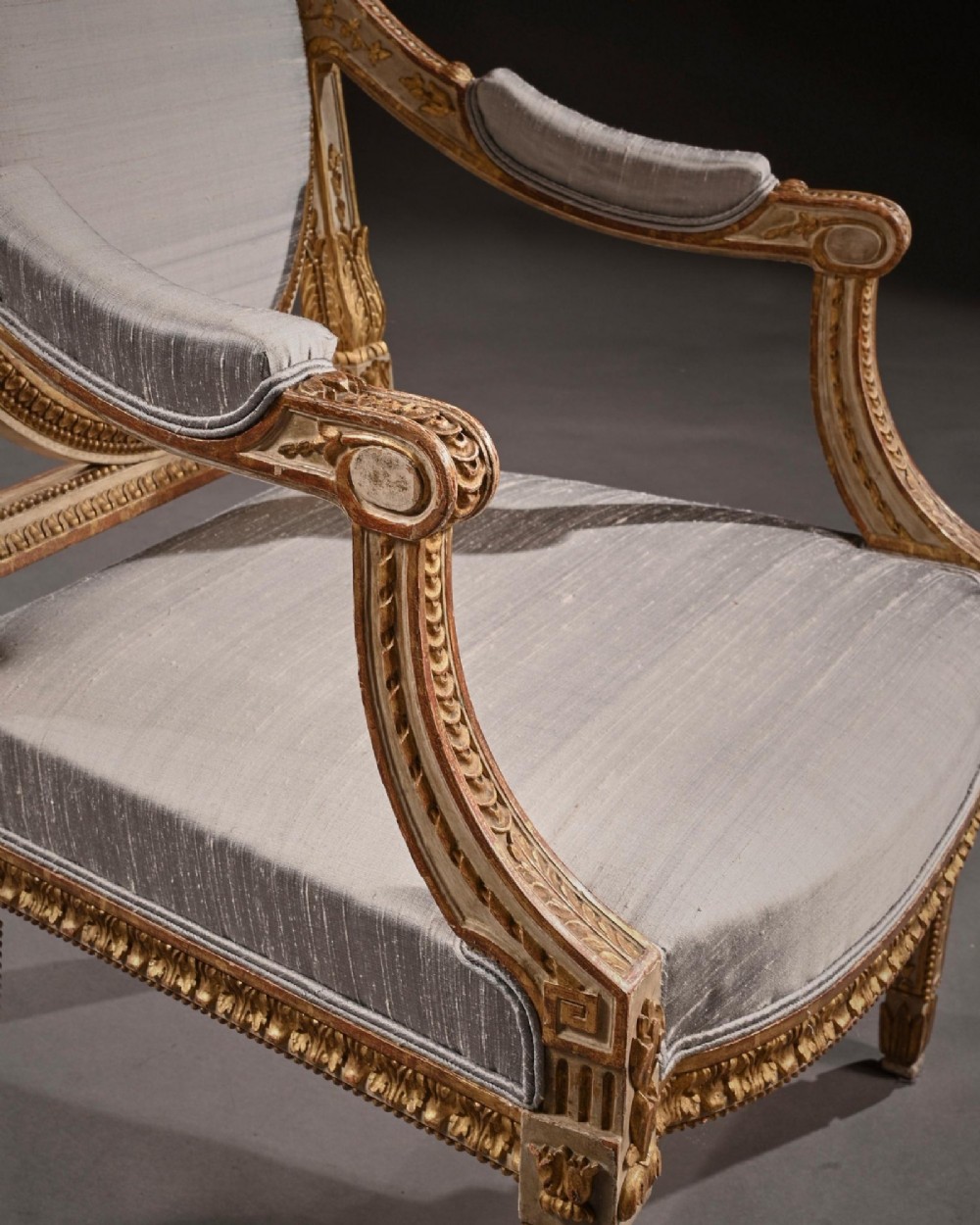 A pair of 19th-century Italian Neoclassical armchairs featuring cream painted and gilt carved frames, oval backrests, and light grey silk upholstery. View X