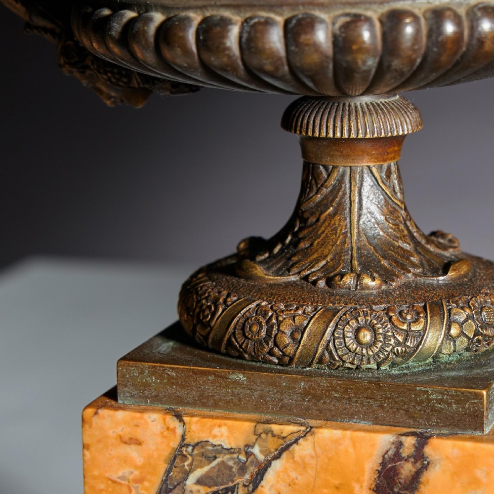 A pair of early nineteenth-century French patinated bronze tazzas with ornate scroll handles mounted on square veined yellow marble plinths. View VI