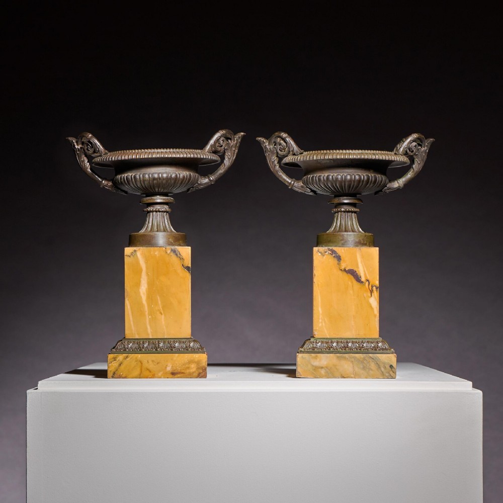 A pair of early 19th-century French Grand Tour bronze tazzas featuring fluted rims and scrolled handles set upon tall yellow Siena marble pedestal bases.