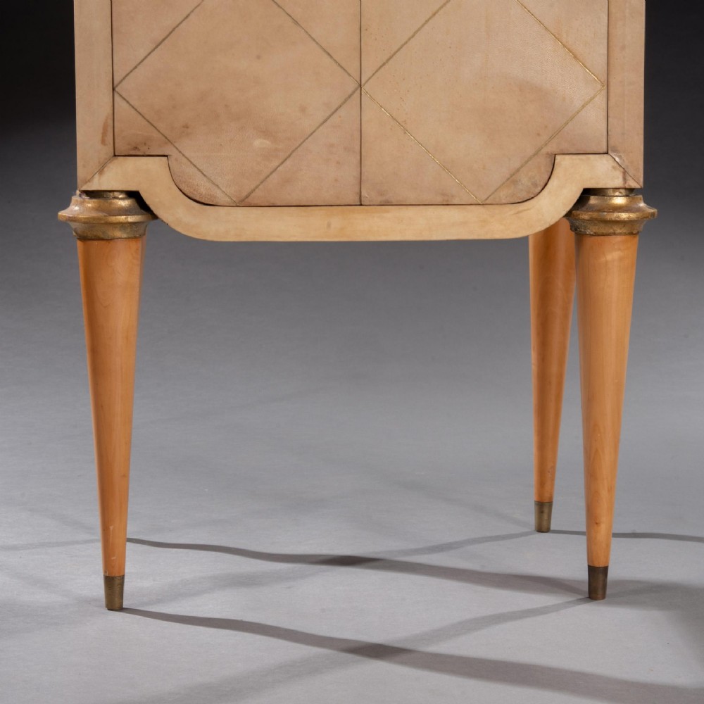 A cream parchment-veneered Art Deco standing cabinet featuring diamond-incised door panels, a central bronze mask handle, and slender tapered legs. View IV