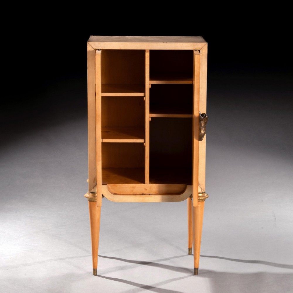 A cream parchment-veneered Art Deco standing cabinet featuring diamond-incised door panels, a central bronze mask handle, and slender tapered legs. View V