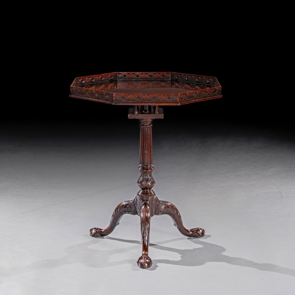 A George III dark mahogany octagonal tripod table featuring a pierced fretwork gallery top, fluted column, and carved legs with claw-and-ball feet.